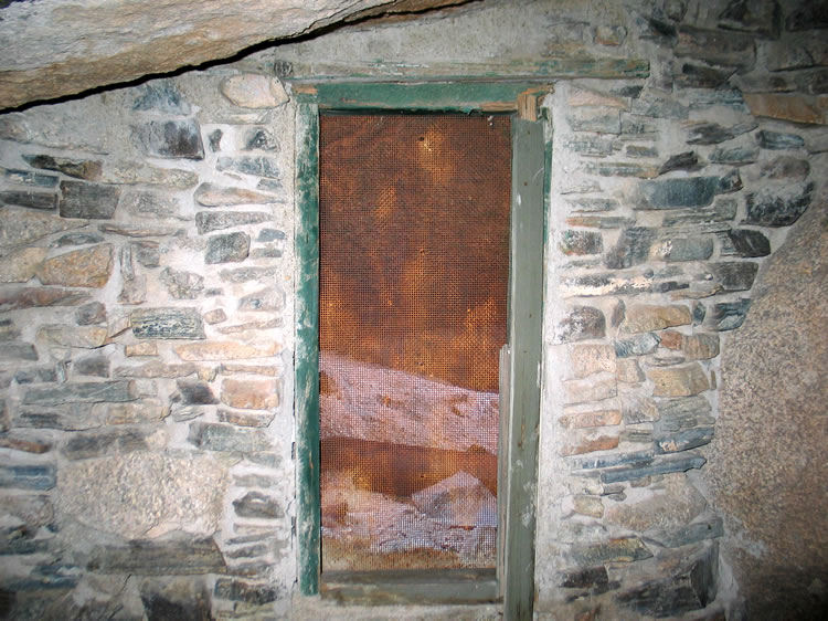 The third window opens onto a sheltered exterior storage area reached from the side of the boulder.