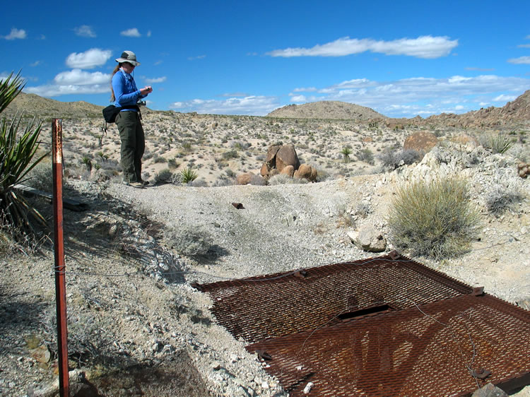 The deep shaft is grated for safety.  Niki takes a GPS reading of the shaft location.