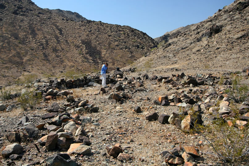 A short distance up canyon from the first stone foundation is another of similar proportions.  Niki is taking a photo of a small decorative embossed tin strip that she found wedged into the rocks.