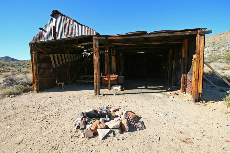 There are two bays.  The one to the left has a picnic table and small chair in it, while the one on the right seems to have been kept clear so that a vehicle could be sheltered inside.  Between the two bays is a stove built from a 55 gallon drum.