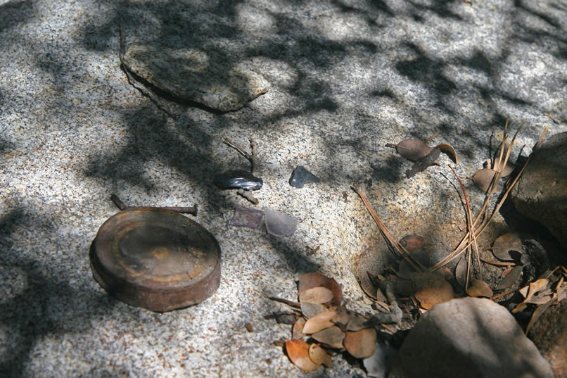 We find an old hole and cap can lid, some purple bottle glass and some obsidian flakes at the shelter.  Notice also the partially filled bedrock mortar to the right of the can lid.