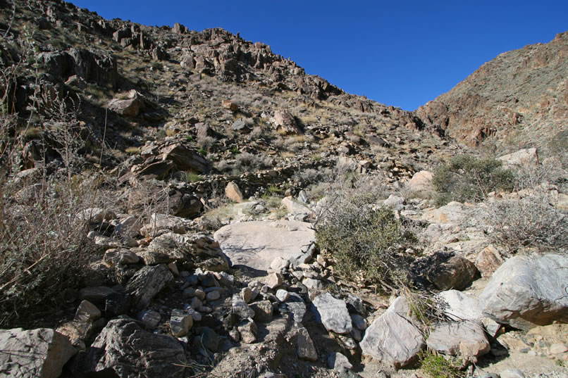 However, rising out of the boulder jumbled wash just a little further along, we can see what looks like a stacked stone shelf  trail and head over to check it out.