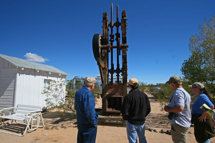 While Guy, Dezdan and Alysia listen attentively, Dennis Casebier shows off the collection of stamp mills that have been salvaged from desert mines.