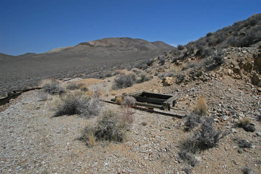 That wooden collar marks the location of a shaft.  In front of the collar is one of the remaining rails for a short set of tracks running over to the ore chute and on to the tailings dump.