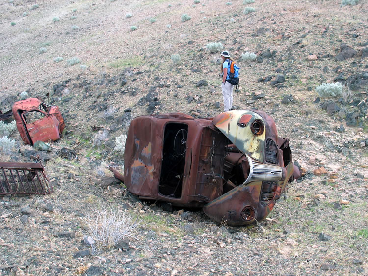 Several rusting car and truck bodies sprawl artistically at the bottom of a small wash.
