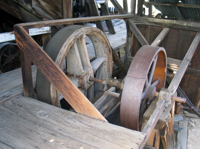 The large wooden wheel to the left, belted directly to the Western gas engine, turns the shaft from which all other equipment is operated.  The iron wheel to the right drives the water pump via its own belt.