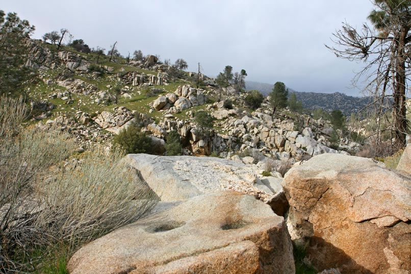 There are two water filled bedrock mortars on the top of the boulder in the foreground.  Between this boulder and the hillside in the distance lies the Kern River in a deep cleft.