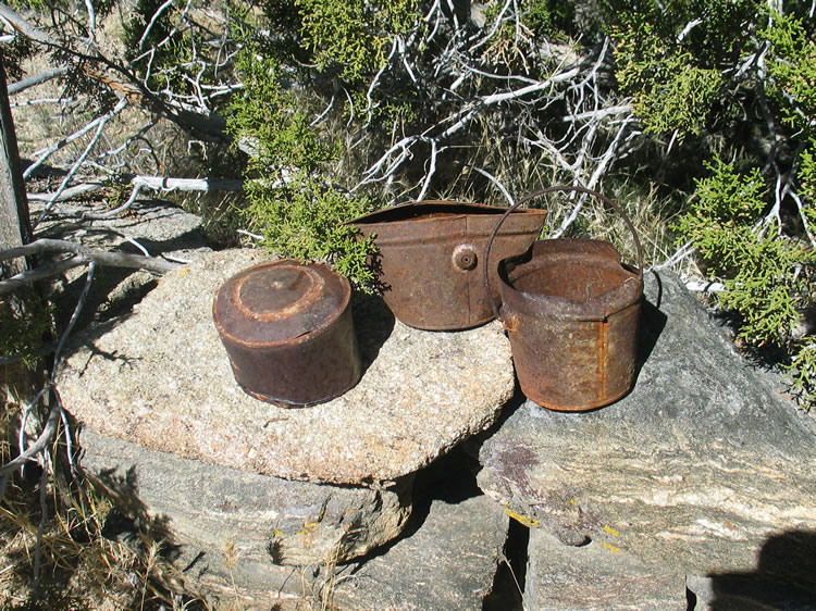 A hole and cap can and two pails on the low rock wall or foundation remnant adjacent to the fireplace.