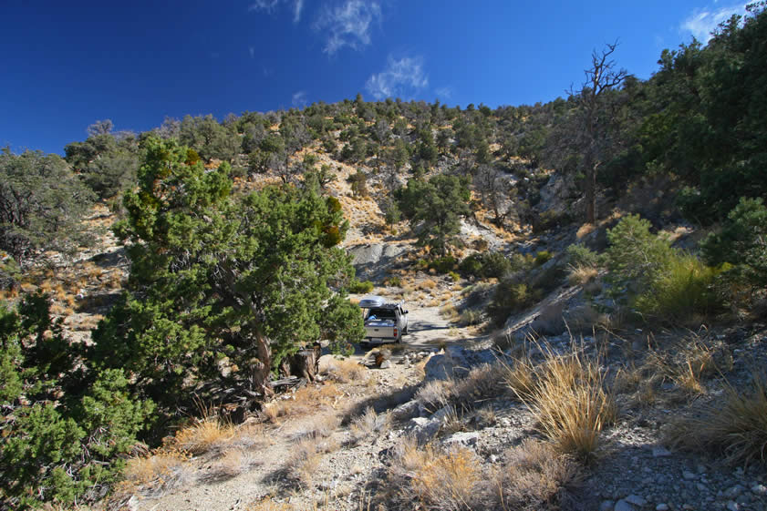 This view from a shallow prospect pit is back toward the truck and beyond it to another tailings pile next to a deep shaft.