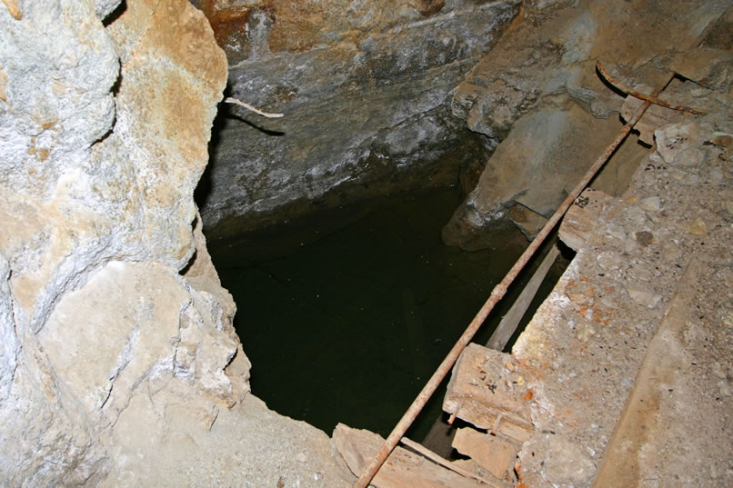 A closer look at the water filled shaft.  The water is so clear that our headlamp beams pierce through it revealing drowned timbers far below the surface.