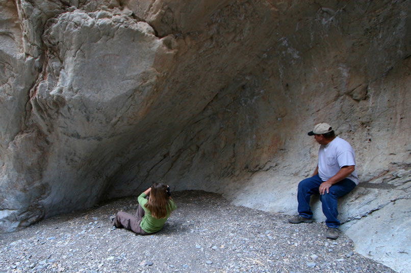 This gouged out stone bowl is literally covered in rock art and seems to have been the most significant site in the canyon.  As the rest of our crew works their way up here, Niki begins to photograph some faint red pictographs on the rock wall to the left of Bill.