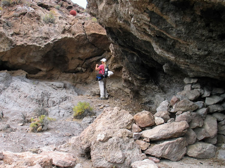 The shelter itself has a stacked rock wall visible in the foreground.  Jamie is taking a photo of an old beehive.