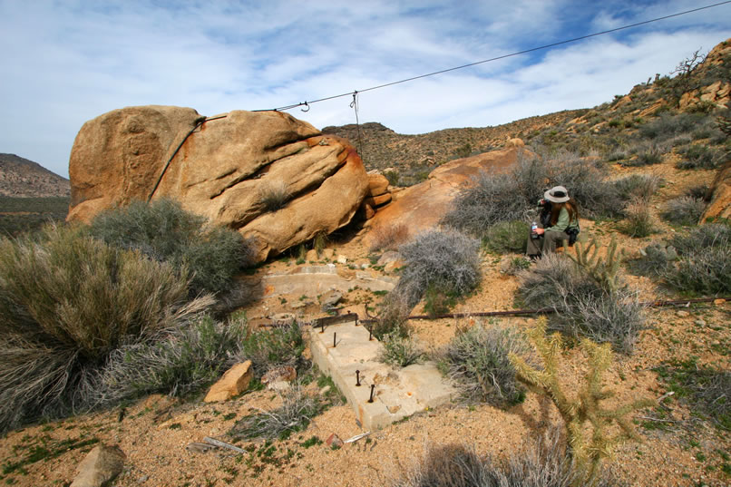 Judging from the equipment pad, this arrastra was motor powered.  Notice also the rusted iron pipe bringing water to it from the stream and the cable lashed around the boulder that was used to lower ore to the arrastra from the workings further up the mountain.